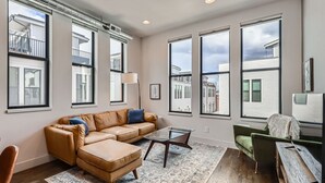 A spacious living room with large windows, a leather sofa, a glass coffee table, and a green armchair.