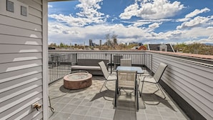 A rooftop patio with a table and chairs, a fire pit, and a view of the city skyline.