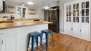 Eine moderne Küche mit weißen Schränken, einem Edelstahl-Kühlschrank, Holz Arbeitsplatten und zwei blauen Barhocker.