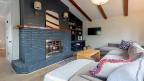 Ein Wohnzimmer mit Kamin aus Backsteinen, einer Couch, einem Couchtisch und einem an der Wand montierten Fernseher.