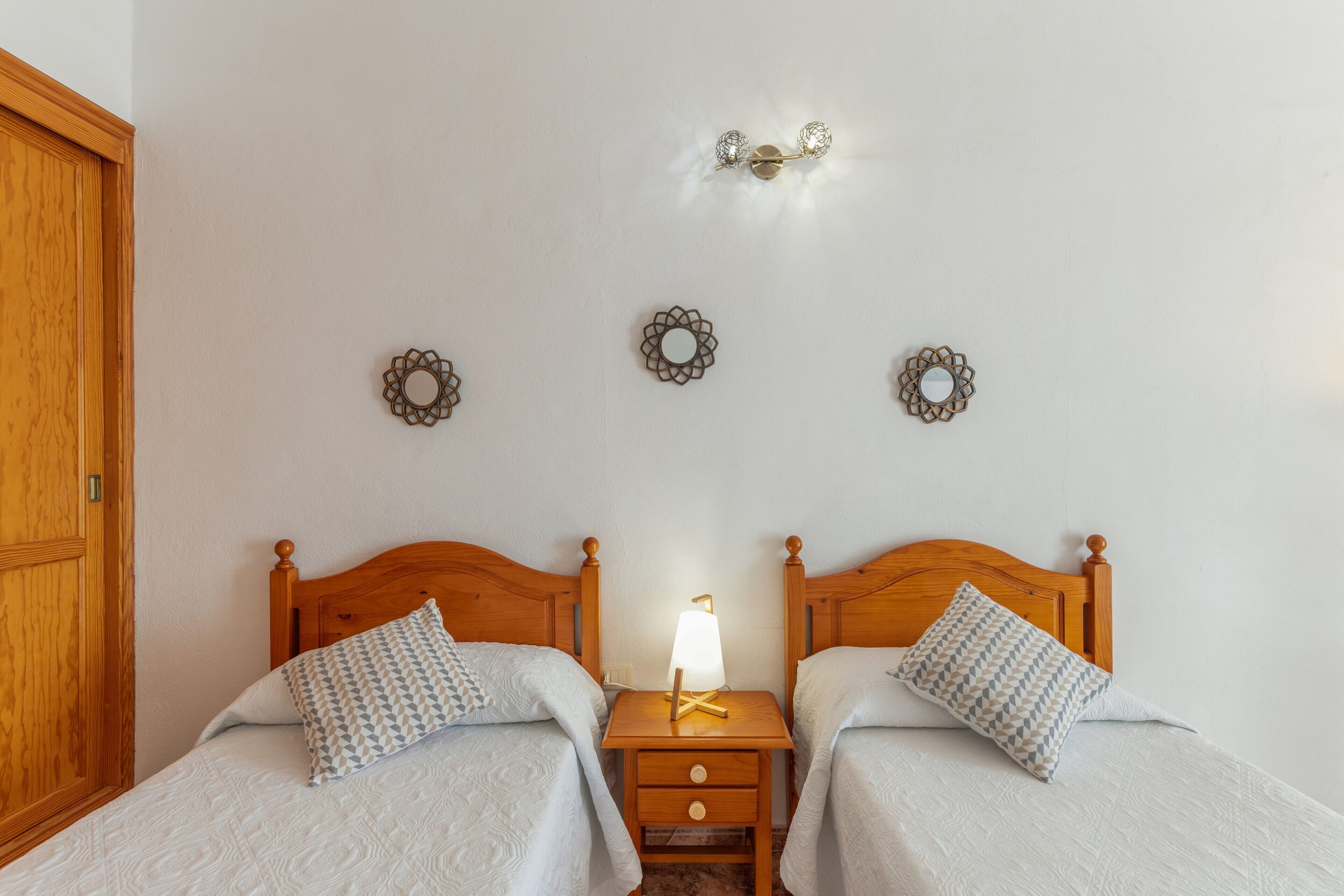 Une chambre à coucher avec deux lits en bois, une table de chevet avec une lampe et des miroirs décoratifs sur les murs.