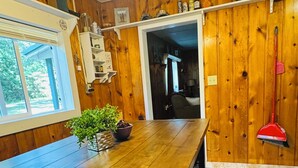 Ein Zimmer mit Holzwandverkleidung, einem Esstisch, einem Deckenventilator, einem Fenster und einer Tür zu einem anderen Raum.