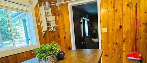 Una habitación con paneles de madera, una mesa de comedor, un ventilador de techo, una ventana y una puerta que da a otra habitación.