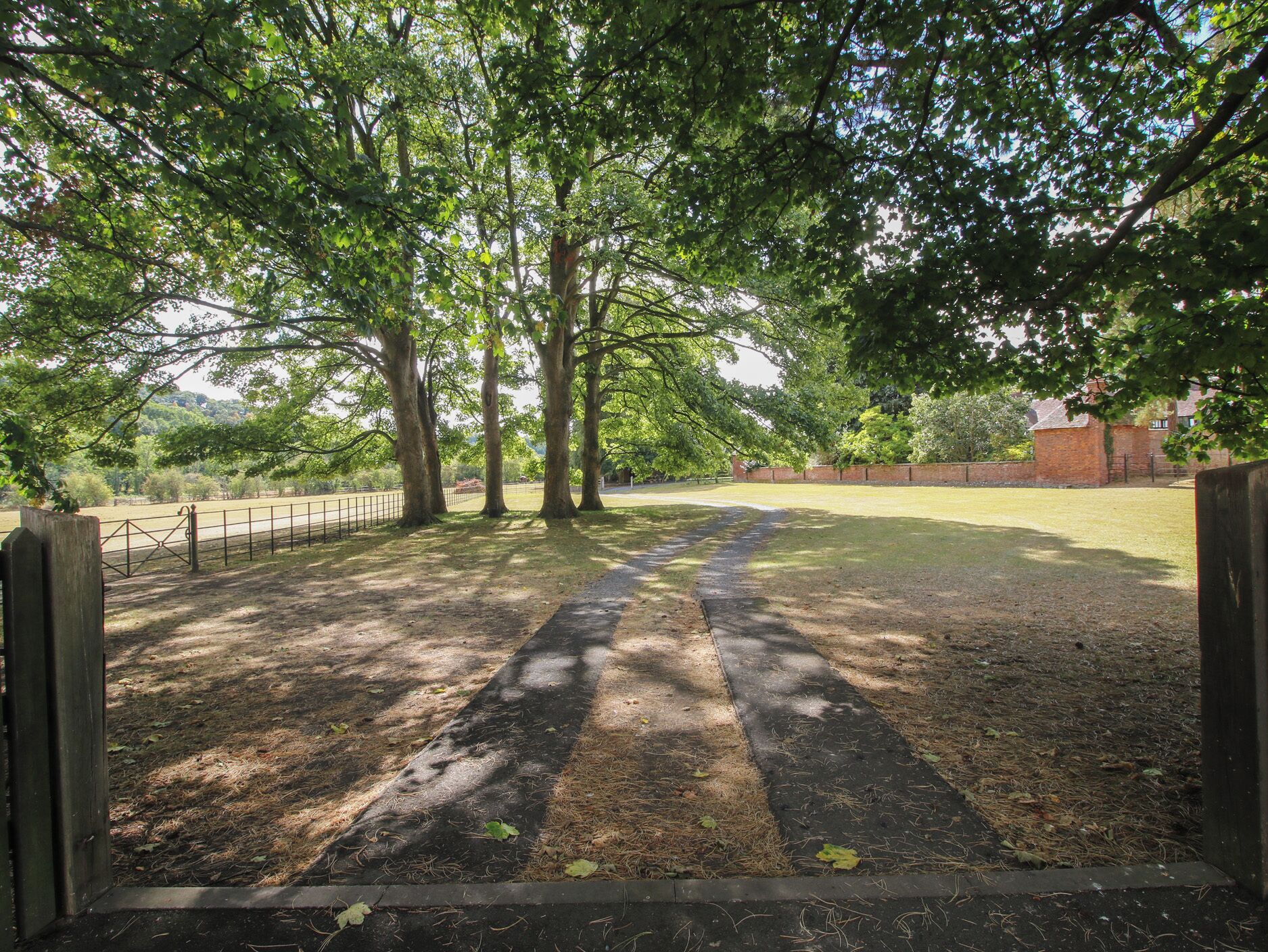 A park with a paved path, trees, and a brick wall in the background.