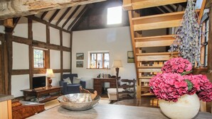A rustic room with exposed wooden beams, a wooden desk, a chair, a television, a lamp, a bookshelf, and a vase with flowers.