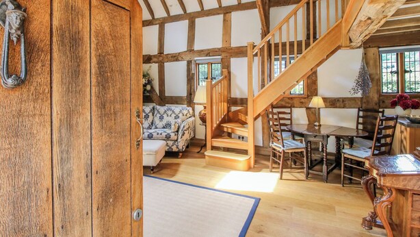 A rustic interior with exposed wooden beams, a wooden staircase, a sofa, a dining table, and a chair.