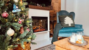 A cozy living room with a fireplace, a Christmas tree, a blue armchair, and a coffee table with candles. - Chalet - Waterfront haven A host of activities for all seasons (Chertsey)