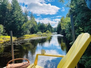 A river view with a chair and a basket, surrounded by greenery and trees.