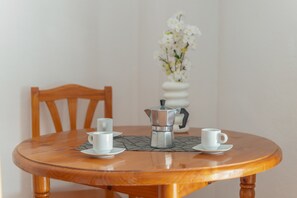 Une table ronde en bois, avec une cafetière et deux tasses, une chaise et un vase rempli de fleurs blanches.