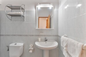 Une salle de bain équipée d’un WC, d’un lavabo, d’un porte-serviettes et d’un miroir avec éclairage.