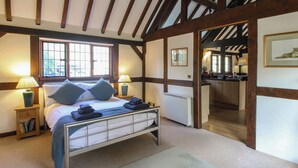 A bedroom with a large bed, a nightstand, a window, and a view into the kitchen. - The Coach House (Church Stretton)