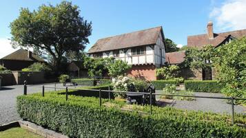 A traditional Tudor-style building with a brick facade and white timber framing, surrounded by well-maintained hedges and a gravel path.