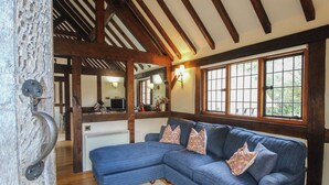A room with a large blue sectional sofa, wooden beams on the ceiling, and a window with a view of greenery. - The Coach House (Church Stretton)