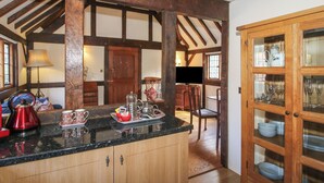 A kitchen with wooden beams, a countertop with kitchenware, and a cabinet with glass doors. - The Coach House (Church Stretton)