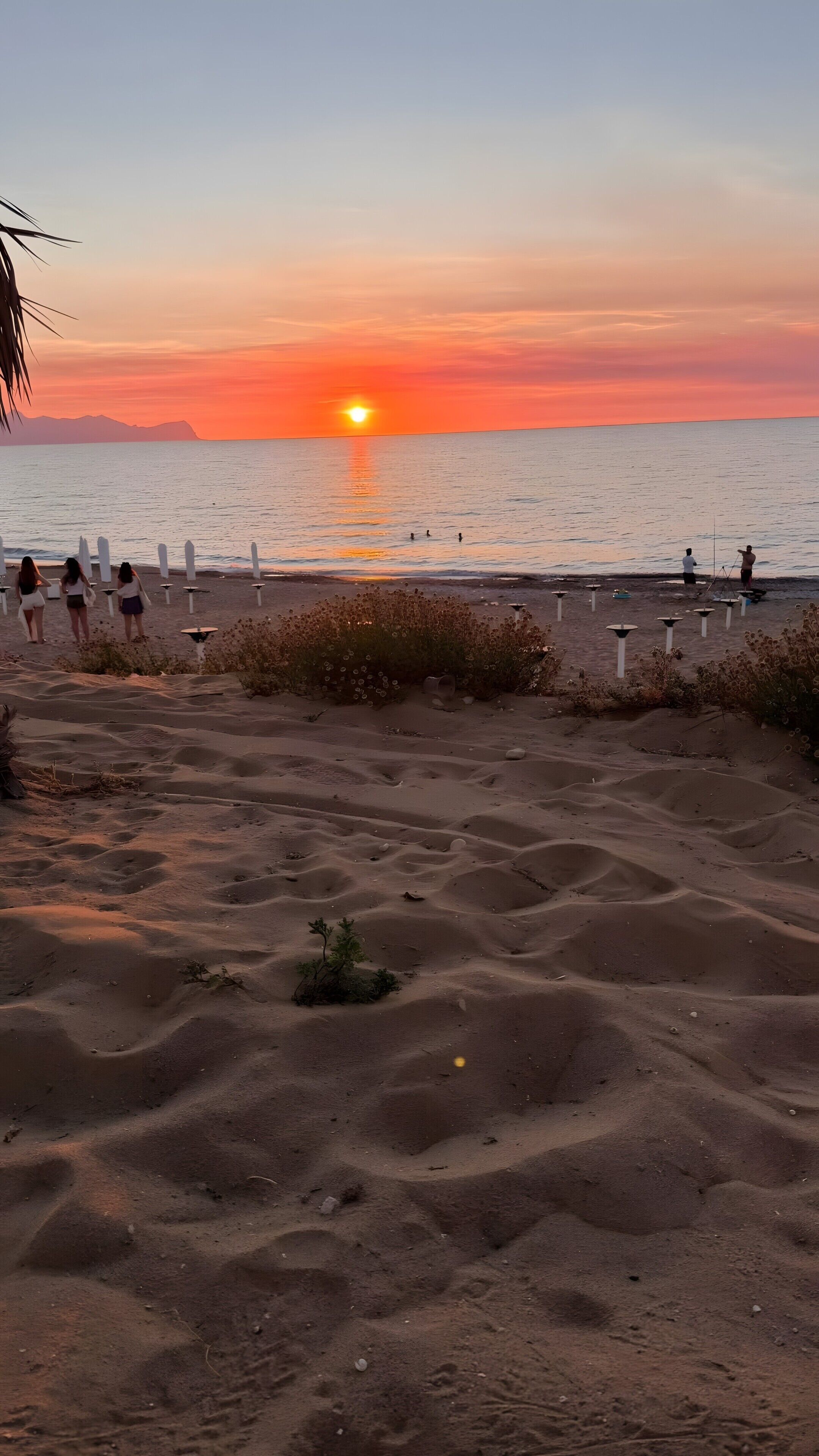Una spiaggia con dune di sabbia, un tramonto e persone in lontananza.