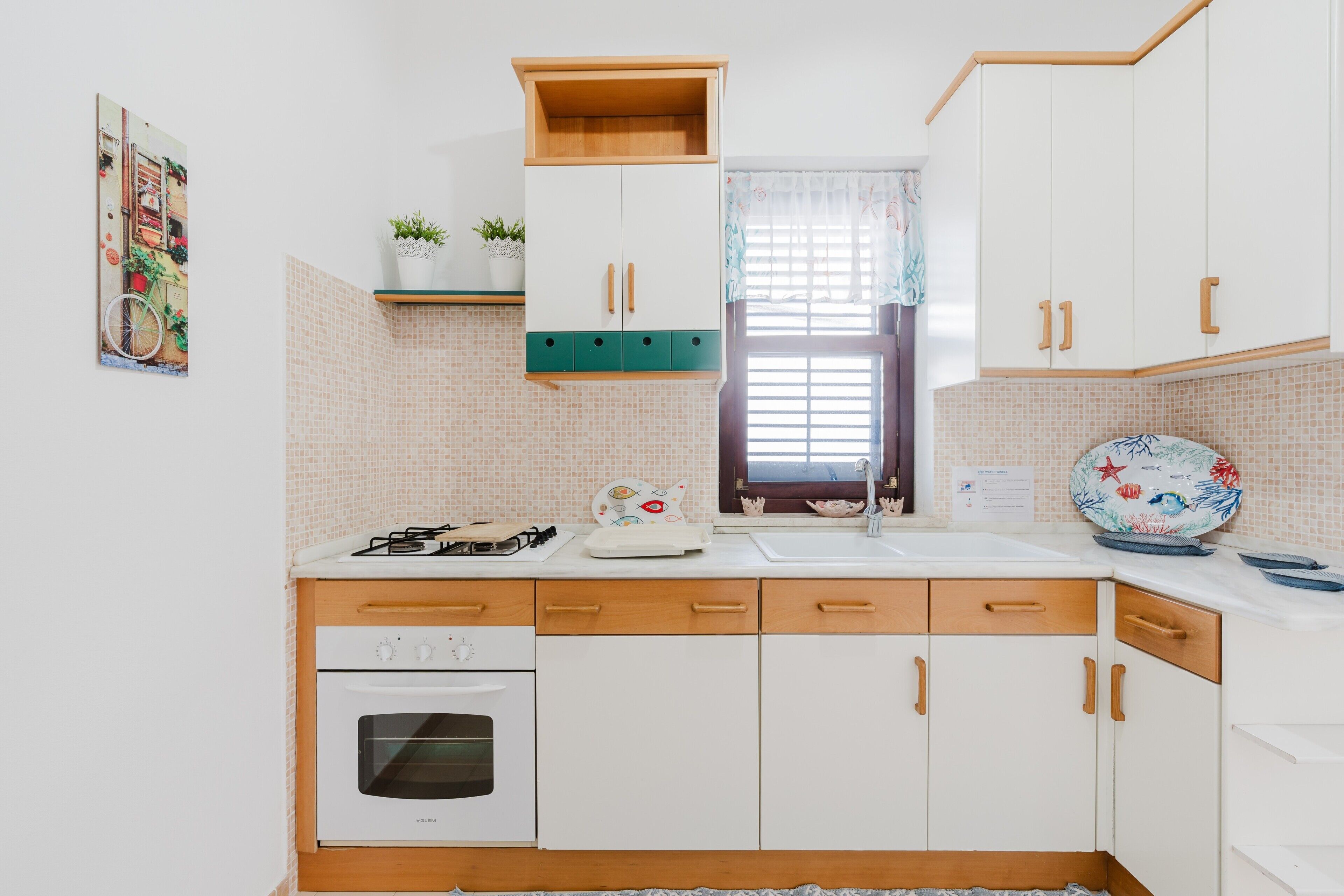 A kitchen with white cabinets, a stove, oven, and a window with a curtain.