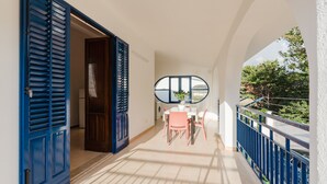 Een balkon met een tafel en stoelen, een blauwe deur en uitzicht op groen.