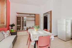 Ett kompakt bostadsutrymme med ett matbord, stolar, en soffa, ett kylskåp och ett skåp med glasdörrar.