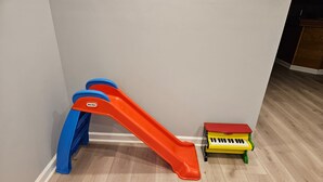 A room with a wooden floor, a red and blue slide, and a small yellow and green toy piano. - Fun 5BR 4.5BA, Pool, Hot Tub, Game Rm, Near O’Hare (Wood Dale)