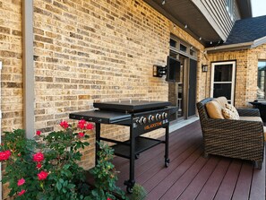 A brick exterior wall with a black grill station and a wicker sofa.