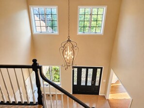 A staircase with a black railing, a chandelier, and a view of a house through a window.
