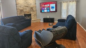 A living room with two sofas, a stone fireplace, a flat-screen TV, and a ceiling fan. - Fun 5BR 4.5BA, Pool, Hot Tub, Game Rm, Near O’Hare (Wood Dale)