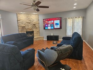 A living room with two sofas, a stone fireplace, a flat-screen TV, and a ceiling fan. - Fun 5BR 4.5BA, Pool, Hot Tub, Game Rm, Near O’Hare (Wood Dale)