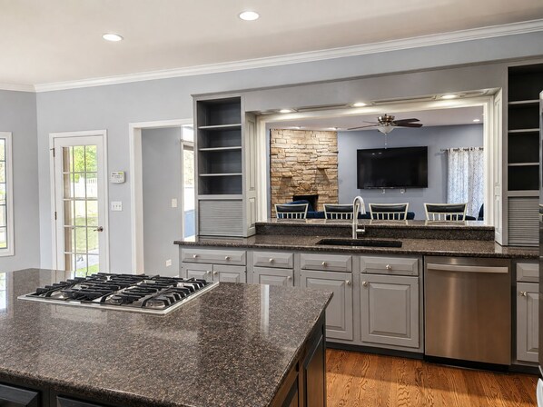 A modern kitchen with a central island, built-in cabinetry, a stone accent wall, and a ceiling fan.