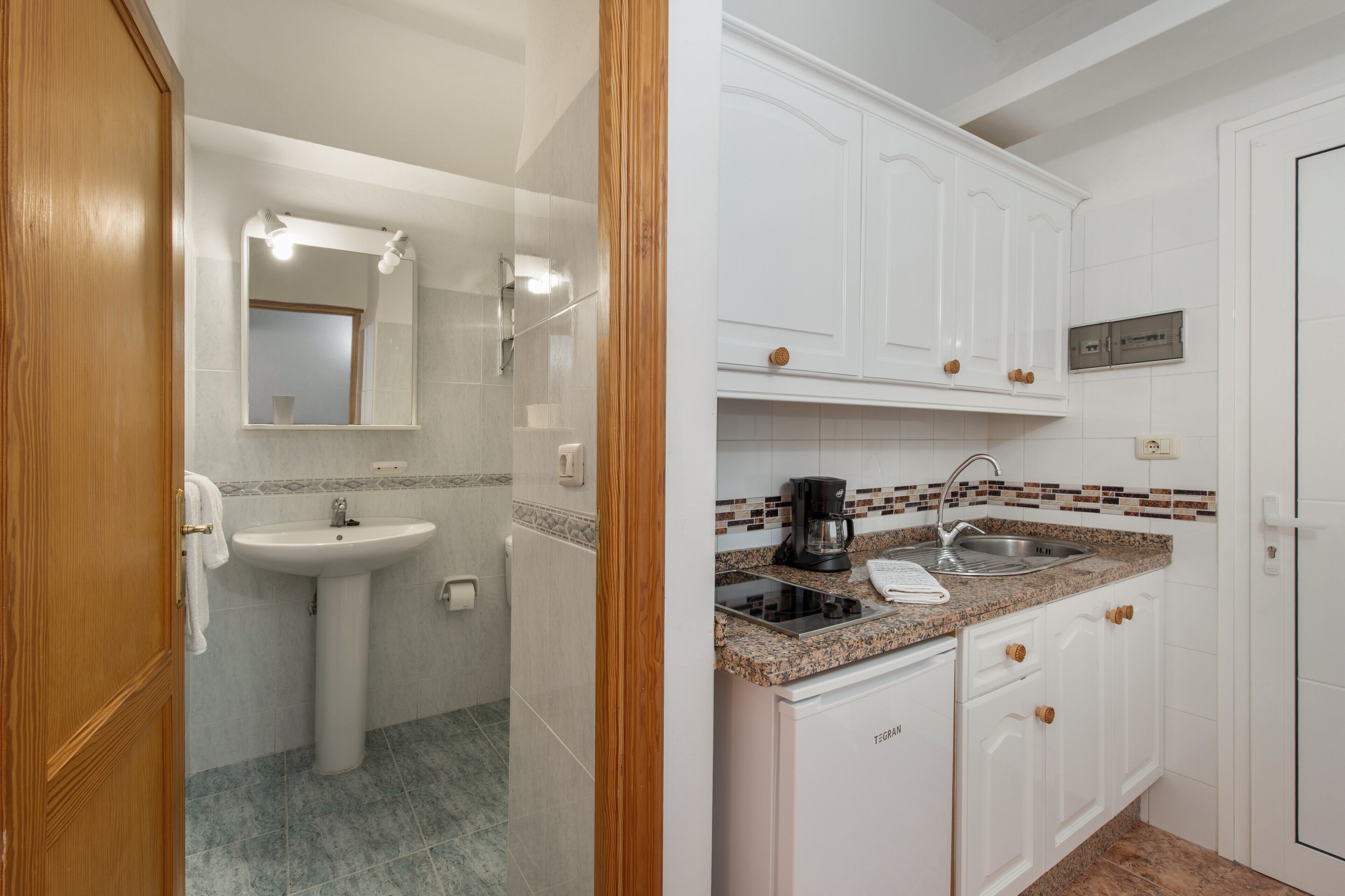 A bathroom with a sink, mirror, and vanity, and a kitchen with cabinets, countertop, and appliances.