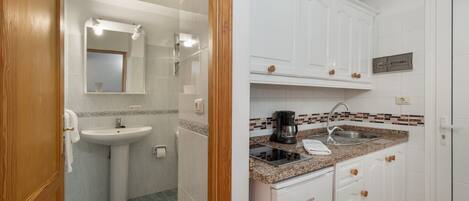 A bathroom with a sink, mirror, and vanity, and a kitchen with cabinets, countertop, and appliances.
