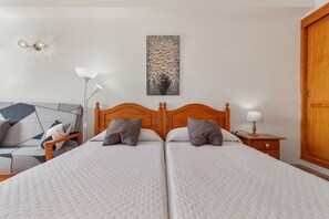 Ein Doppelbett mit Holz-Kopfteil, ein Nachttisch mit Lampe, ein an der Wand hängendes Kunstwerk und ein Sofa mit geometrischem Muster.
