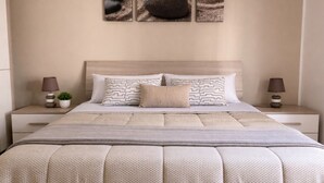 Ein ordentlich eingerichtetes Schlafzimmer mit einem Bett, zwei Nachttischen, einer Lampe, einer Zimmerpflanze und einem an der Wand hängenden Kunstwerk.