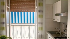 Eine moderne Küche mit Einbauherd, ein Essbereich mit Tisch und Stühlen sowie ein Balkon mit Streifenmarkise.