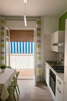 Una cocina moderna con estufa integrada, un comedor con mesa y sillas, y un balcón con toldo a rayas.