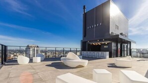 En tagterrasse med moderne hvide møbler, et barområde og udsigt over byen.