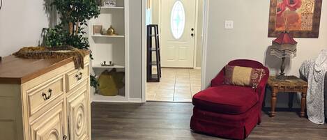 A spacious living area with a wooden floor, a red sofa, a cream-colored cabinet, and a potted plant.