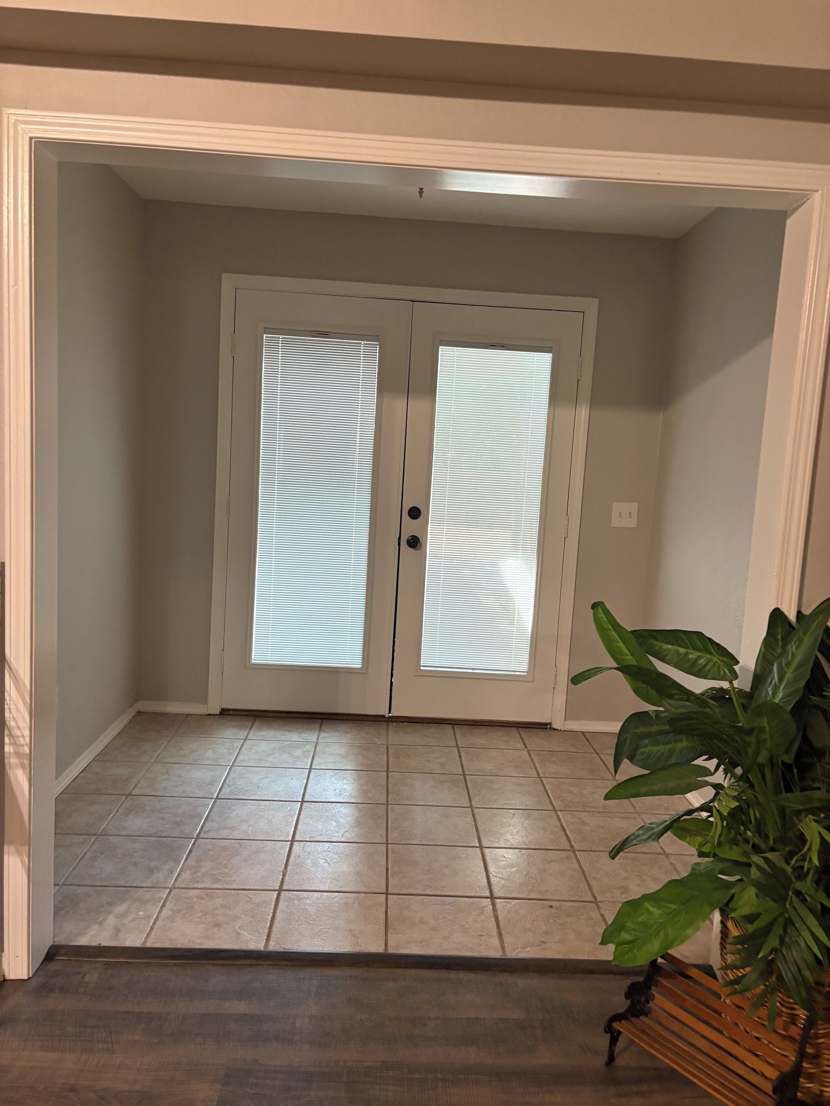 Quarto com porta dupla, piso ladrilhado e planta em vaso.