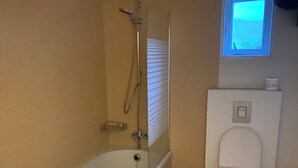 Un baño con bañera, inodoro y una ventana sobre el inodoro.