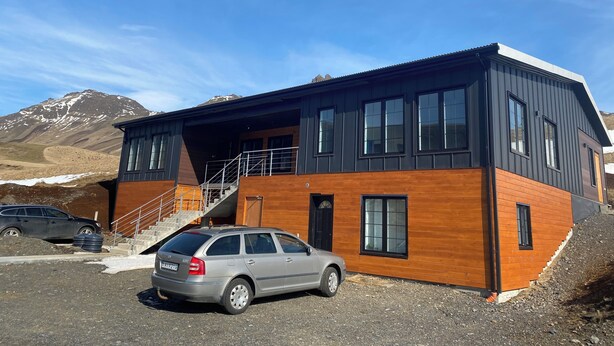 Un moderno edificio de dos pisos con fachada de madera y ventanas amplias, situado en una zona montañosa.
