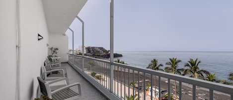 A balcony with white chairs, a small table, and potted plants.
