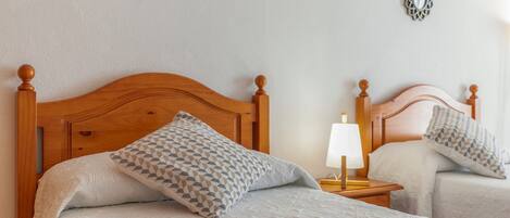 Una cama doble con cabecera de madera, un cojín estampado, una mesita de noche con lámpara y espejos decorativos en la pared.