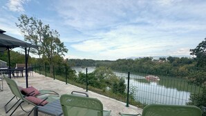 Un espacio al aire libre con sillas y una mesa, con vista a un río y una embarcación.