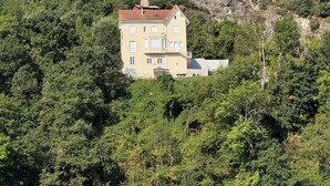 Un edificio de varios pisos rodeado de un bosque frondoso, con un balcón y una chimenea a la vista.