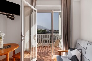 Een balkon met een tafel en stoelen, een bank en een aan de muur bevestigde televisie.