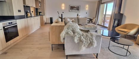 A modern living space with a kitchen, a sofa with a fur throw, a round coffee table, and a fireplace.