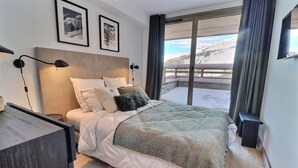 Habitació d'hotel moderna amb un llit gran, vista a un paisatge nevado a través d'un balcó, i quadres a la pared.