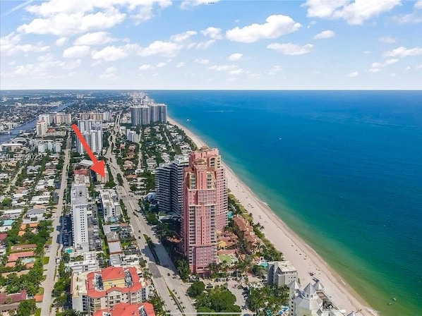 An aerial view of a coastal city with a prominent high-rise hotel building, a beachfront, and a dense urban area with various buildings.