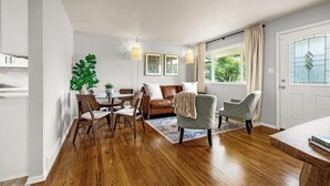 A spacious living area with a wooden floor, a dining table with chairs, a sofa, and a large window with curtains. - New Adventure Cottage w/ Mountain Views Near Garden of the God's and much more! (Colorado Springs)