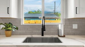 A kitchen with a double sink, white cabinets, a window with a view of a house and a yellow fence, and a potted plant on the counter. - New Adventure Cottage w/ Mountain Views Near Garden of the God's and much more! (Colorado Springs)