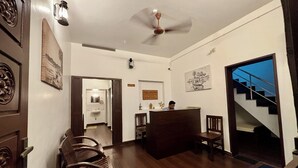 A reception area with a desk, chairs, a ceiling fan, and a staircase. - Fort Grande Stay  (Kochi)